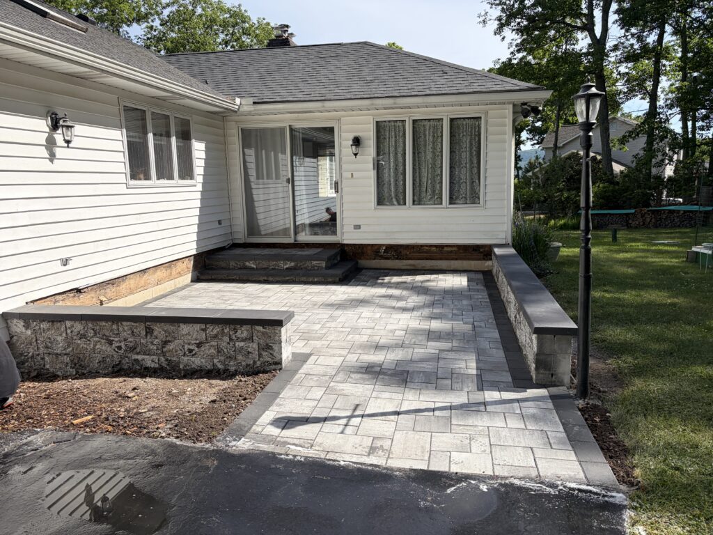 Gray paver walkway leading to a raised patio and front steps